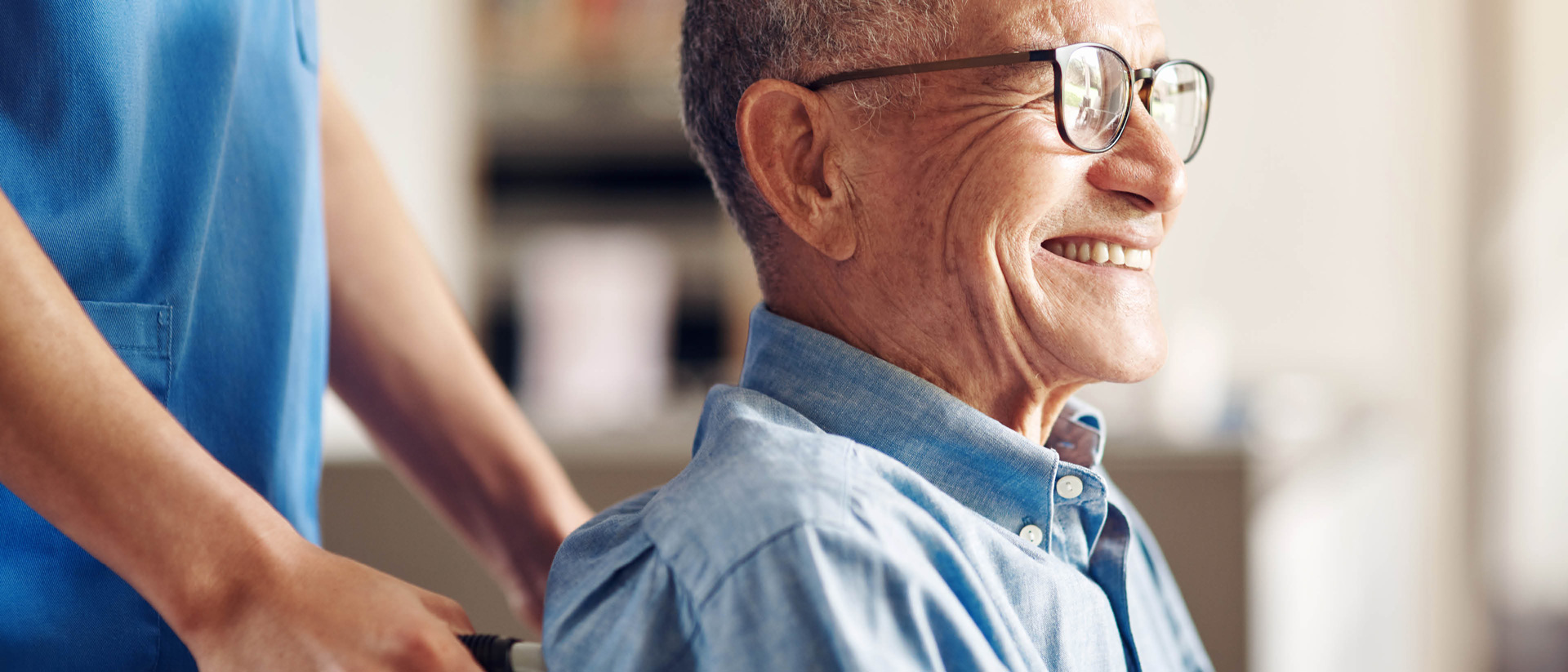 old man with glasses being pushed in wheelchair by nurse