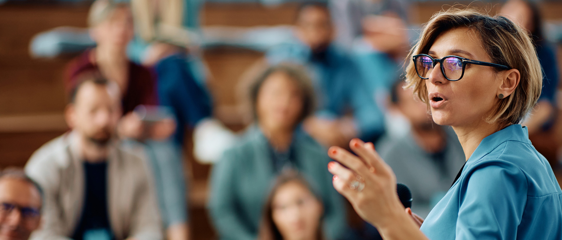 Woman wearing glasses, presenting to a room of people