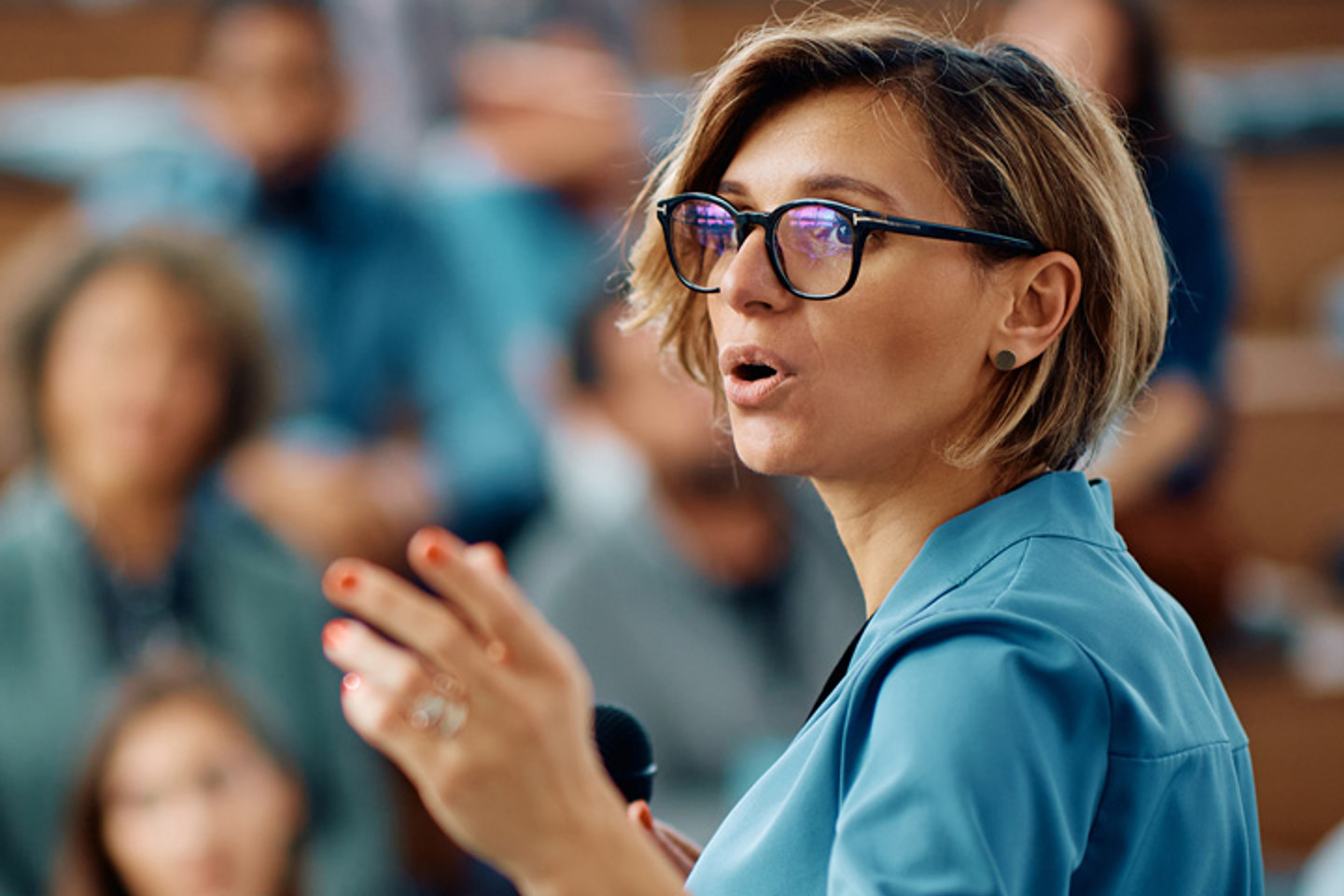 Woman wearing glasses, presenting to a room of people