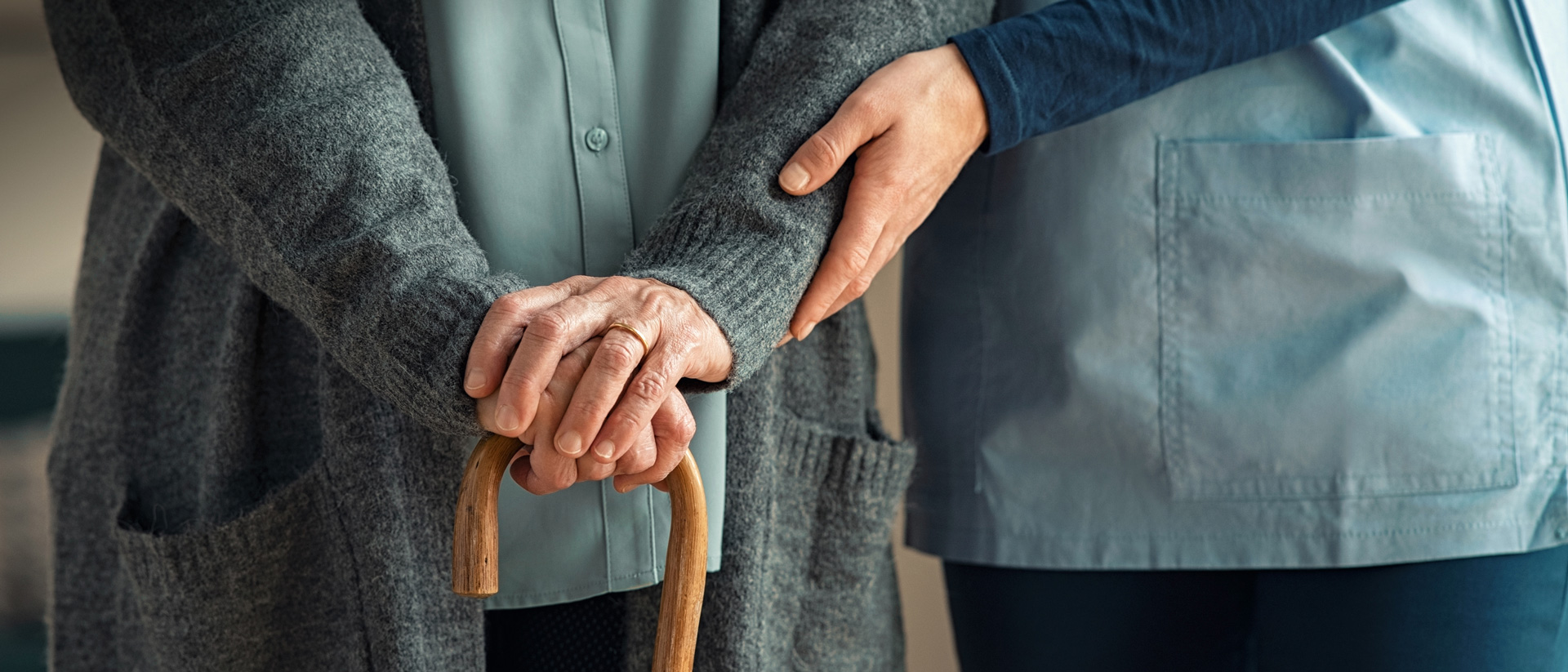 Older man with cane receiving assistance from care worker